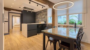 A modern kitchen with dark cabinetry, a central island, and a dining area with a glass table and black chairs. - Modern and Luxurious in Historic Old Town (Bilbao)