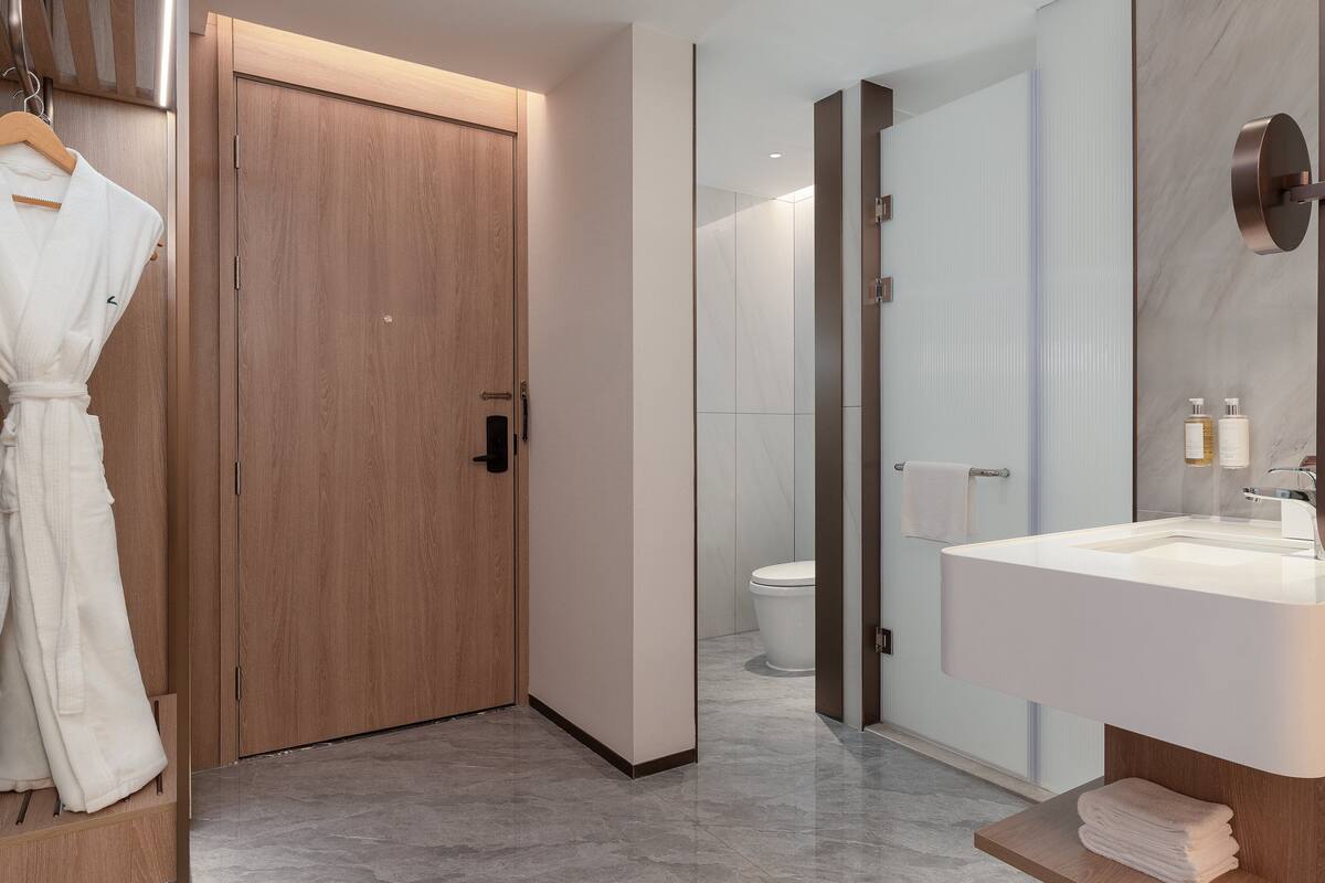 A modern bathroom with a wooden door, a white sink, and a large mirror.