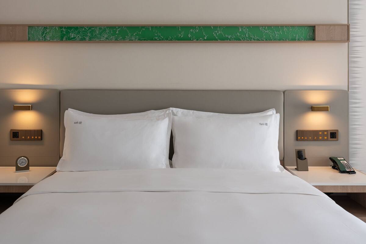 A hotel room with a large bed, two bedside tables, a green accent wall, and wall-mounted lighting.