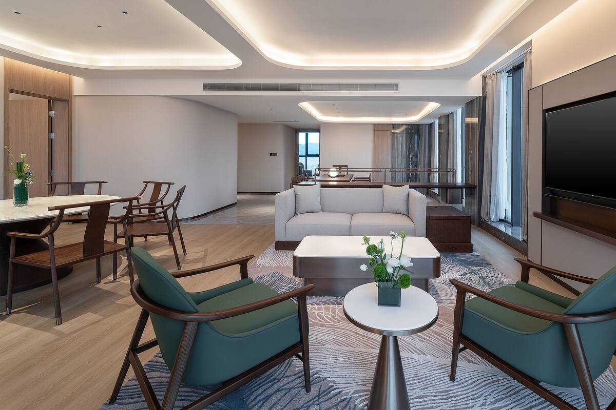 A modern living room with a sofa, chairs, a coffee table, and a TV mounted on the wall.