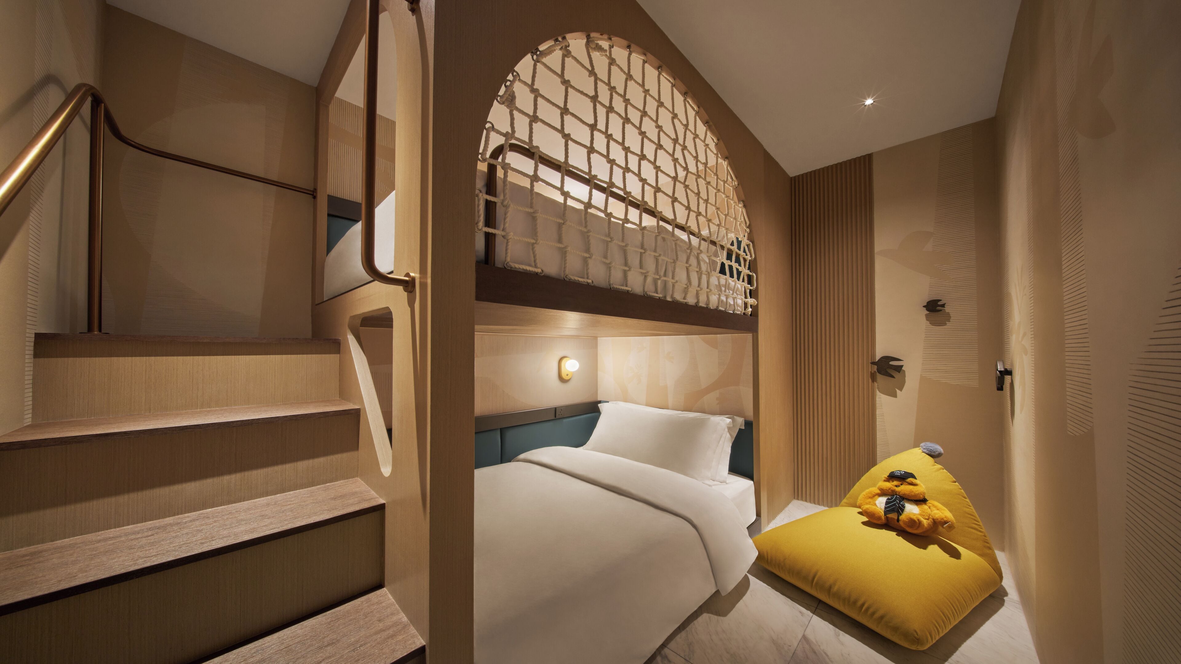 A hotel room with a bed, a small yellow ottoman, a staircase, and a wall with a geometric pattern.