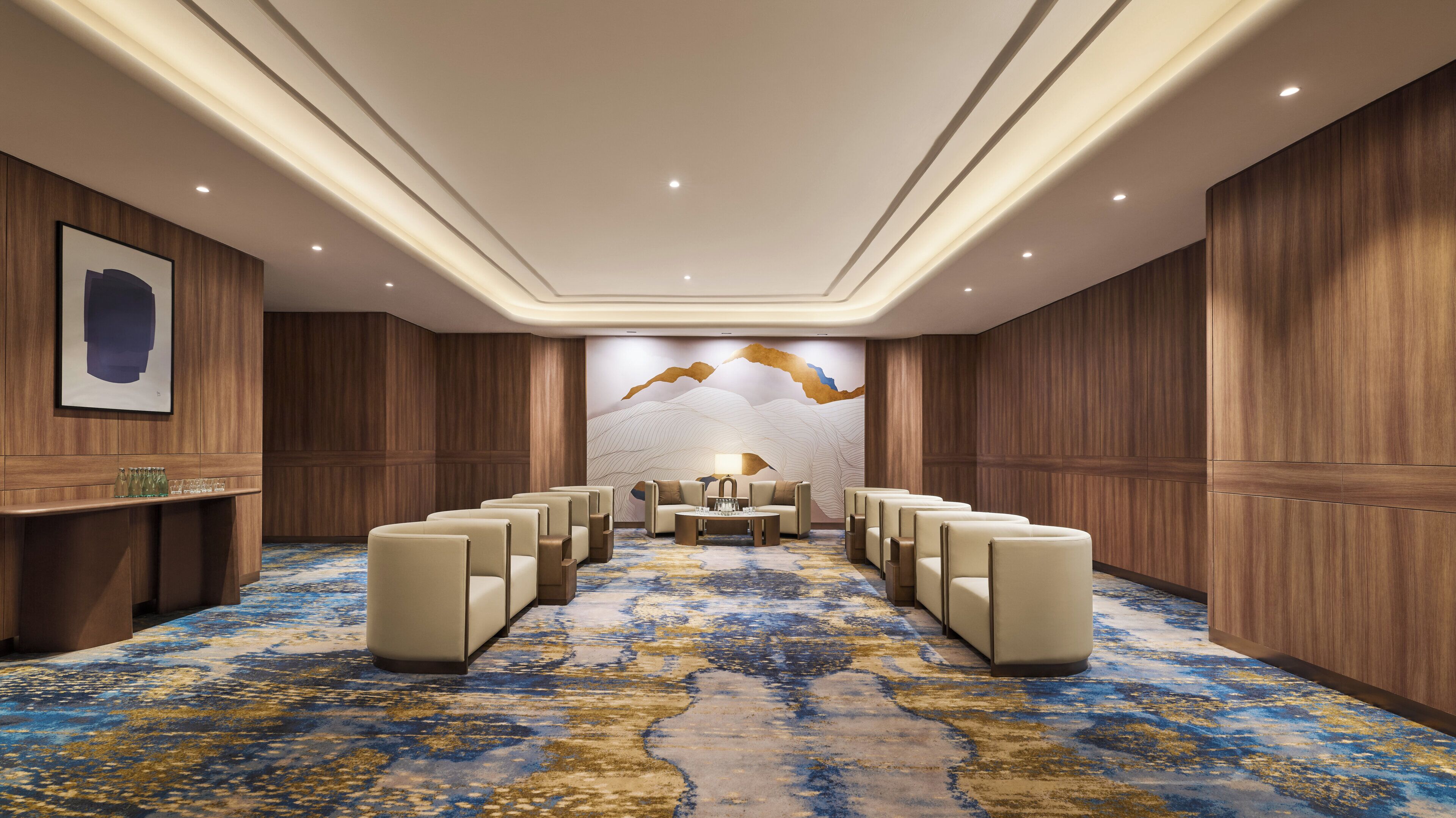 Un salón de conferencias de hotel con una larga mesa, múltiples sillas, paneles de madera y piso alfombrado.