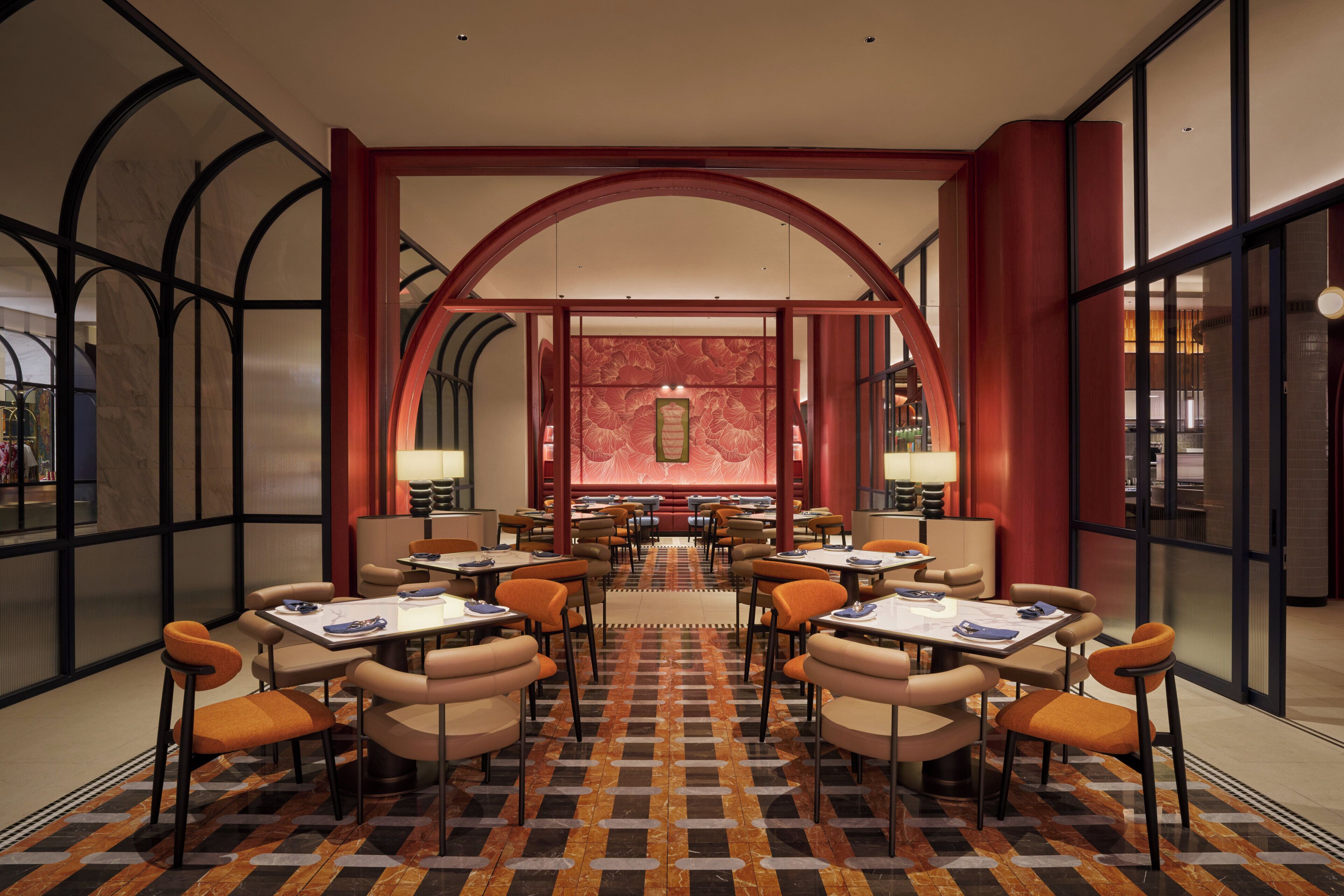A hotel dining area with tables and chairs arranged in a symmetrical layout, large windows on the sides, and a patterned floor.