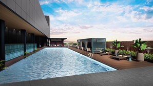 A rooftop pool area with a modern pool, lounge chairs, and a seating area with a view of the sky. - Voco Kuching by IHG (Kuching)