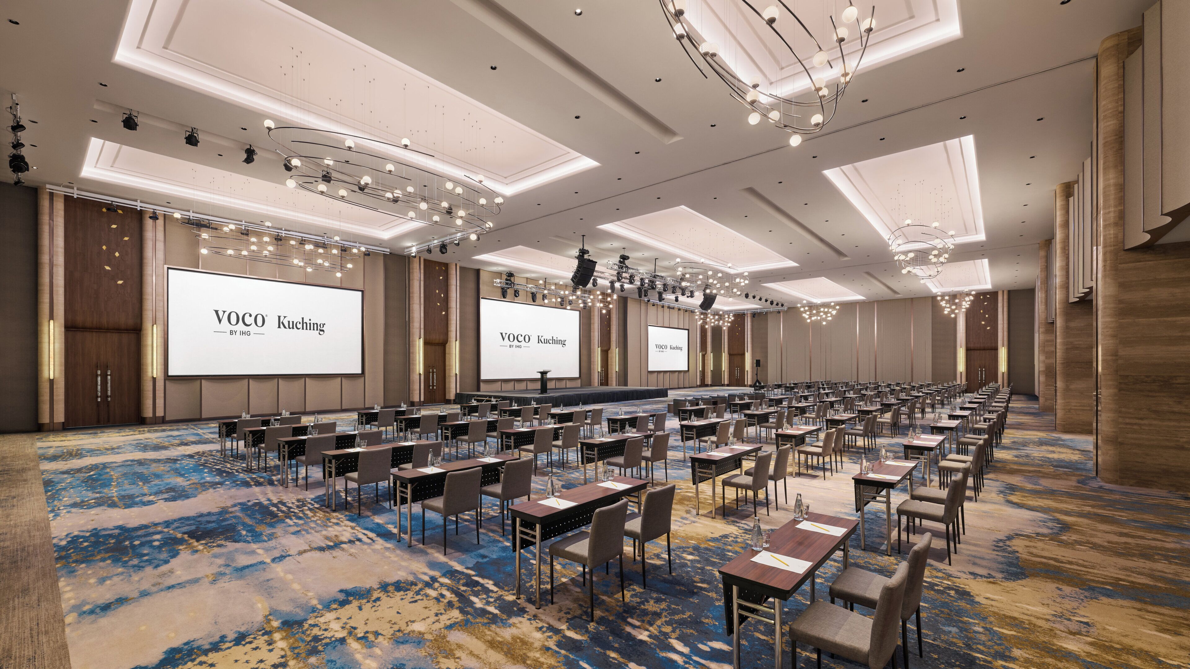 A conference room with multiple tables and chairs, large screens displaying text, and a chandelier.