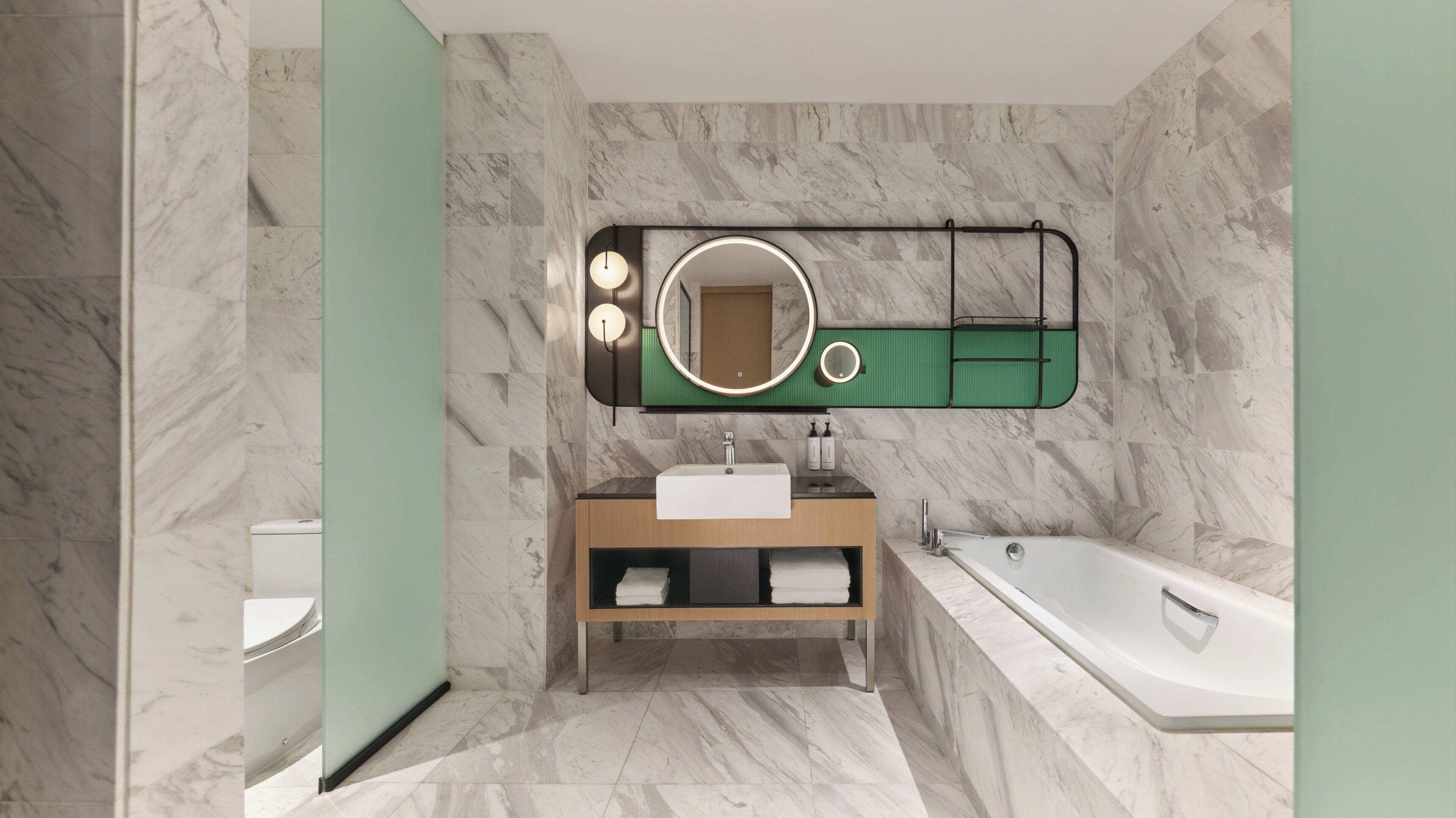 A modern bathroom with a marble floor, a freestanding bathtub, a vanity with a mirror, and a toilet.