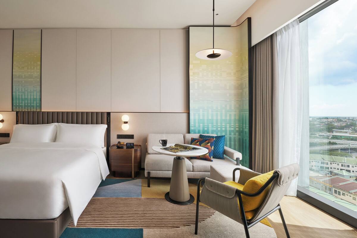 A modern hotel room with a large bed, a seating area with a table, and a city view.