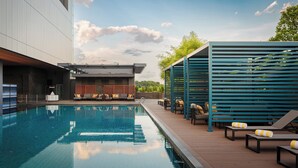 A swimming pool with lounge chairs and a modern building in the background. - Voco Kuching by IHG (Kuching)