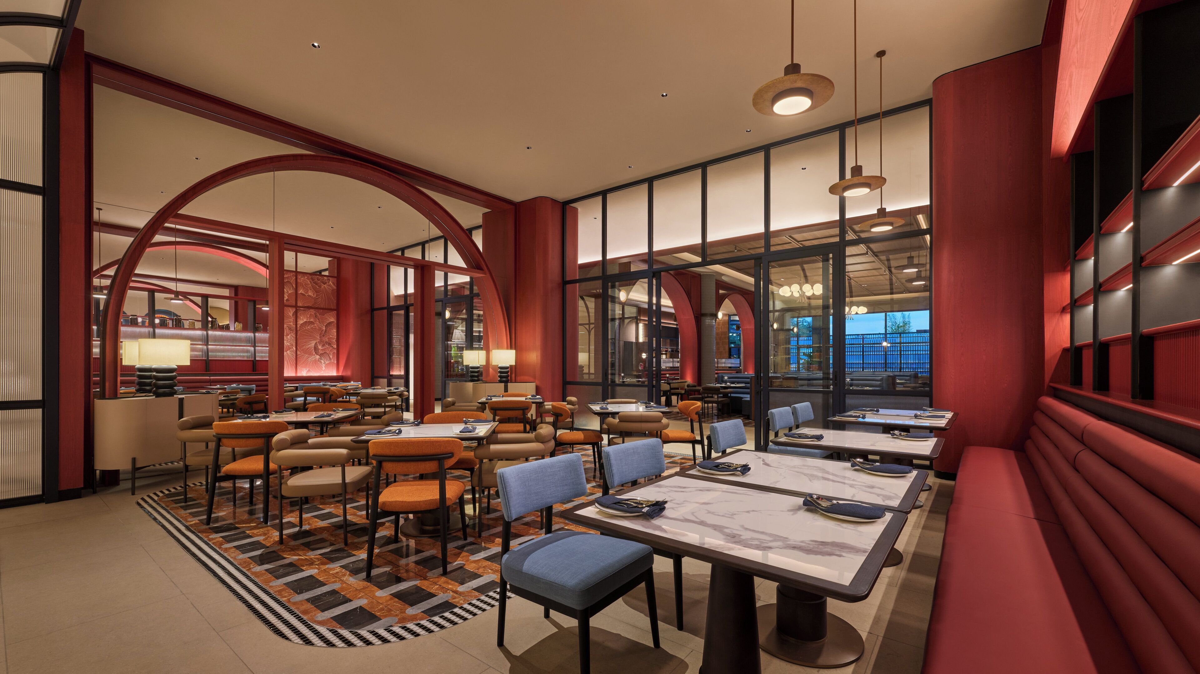A modern restaurant interior with high ceilings, red accents, and a mix of seating arrangements including tables and booths.