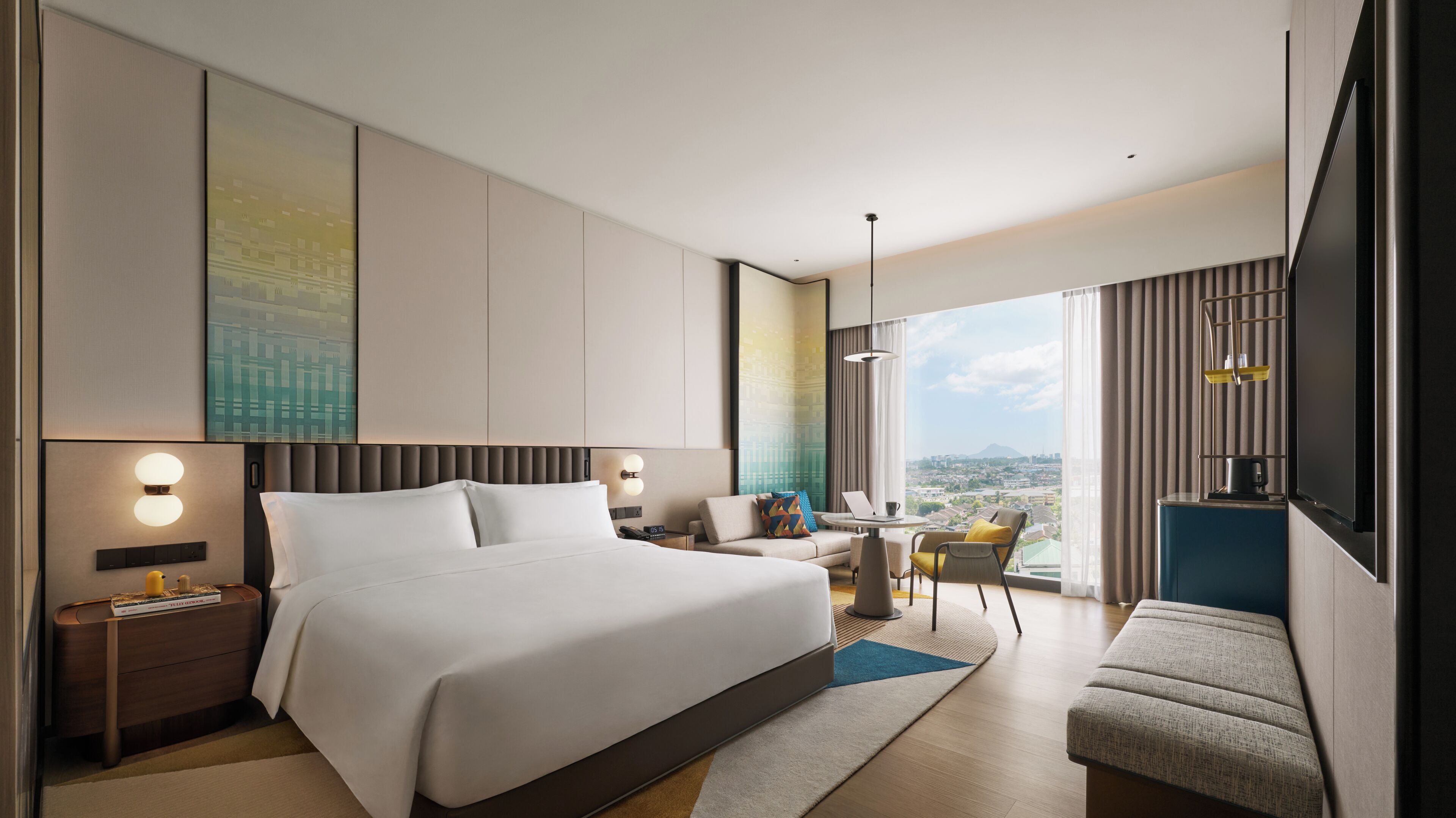 A modern hotel room with a large bed, a desk, and a view of the city.
