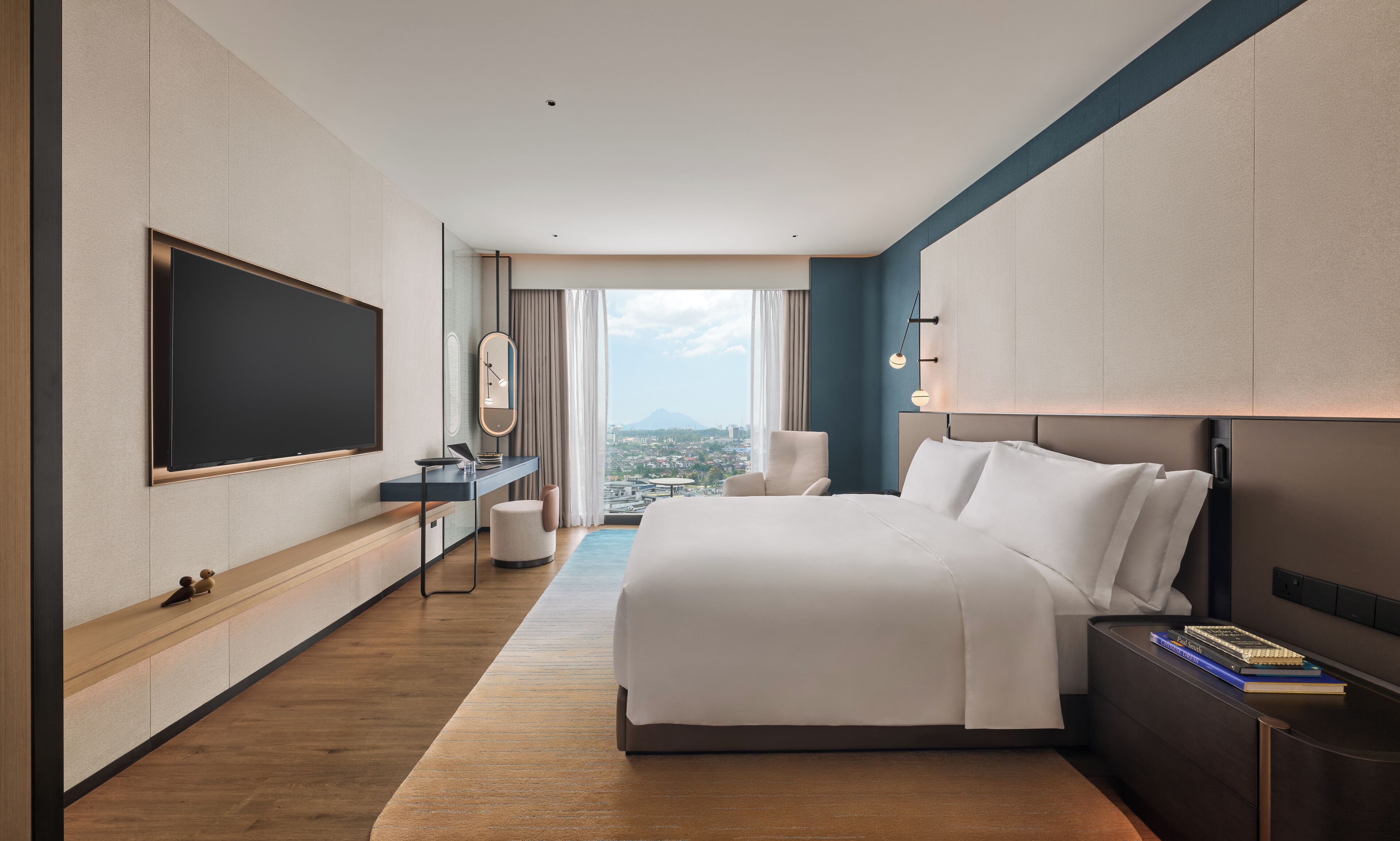 Habitación de hotel moderna con una cama grande, un escritorio con computadora, televisor de pantalla plana y vista a la ciudad.