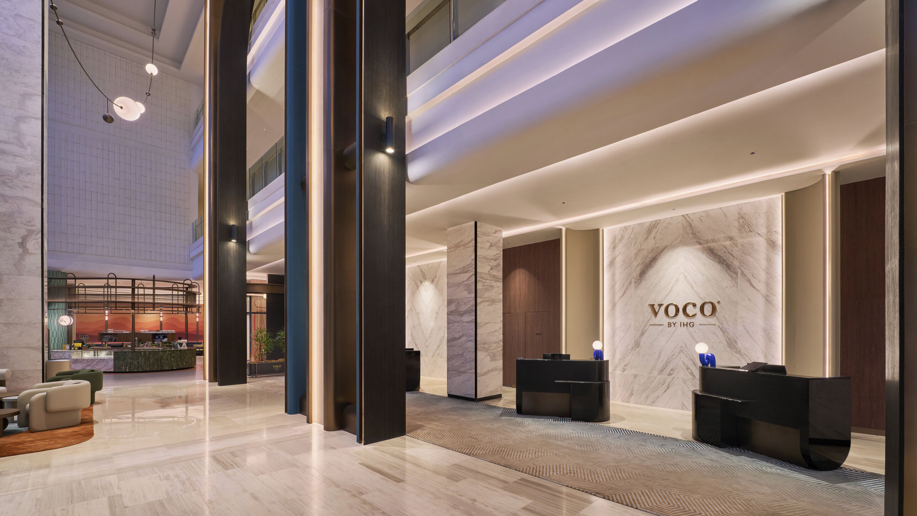 A modern hotel lobby with a reception desk, seating area, and a large marble wall with the hotel name.