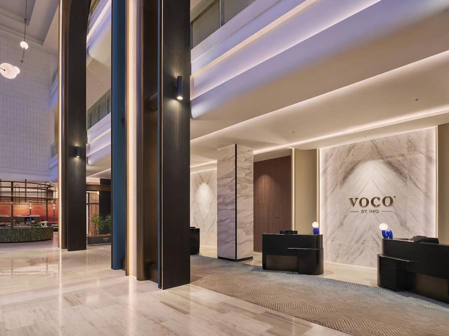 A modern hotel lobby with a reception desk, seating area, and a large marble wall with the hotel name.