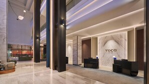A modern hotel lobby with a reception desk, seating area, and a large marble wall with the hotel name. - Voco Kuching by IHG (Kuching)