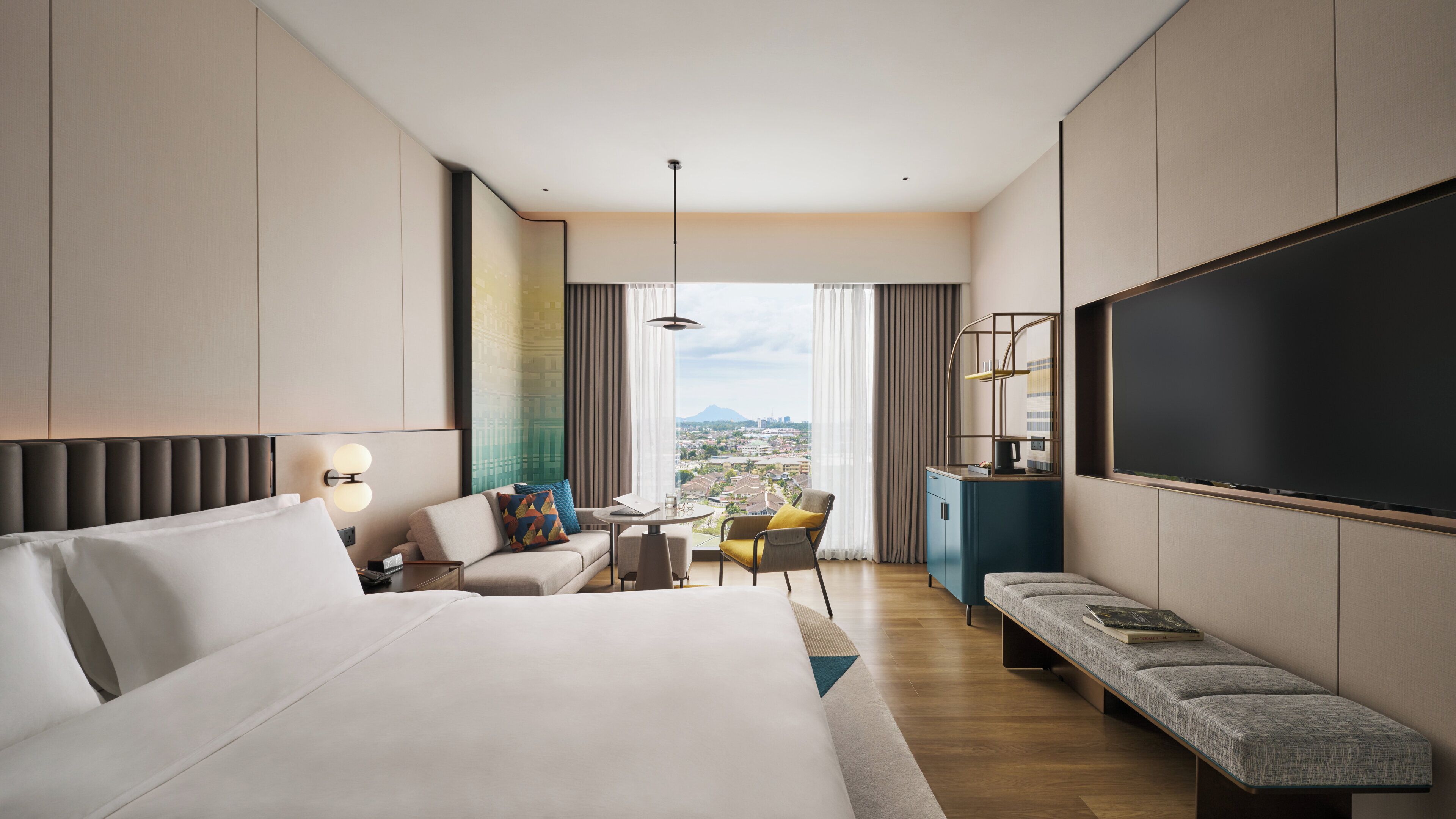 A hotel room with a large bed, a desk, a chair, a sofa, a TV, and a view of a cityscape.