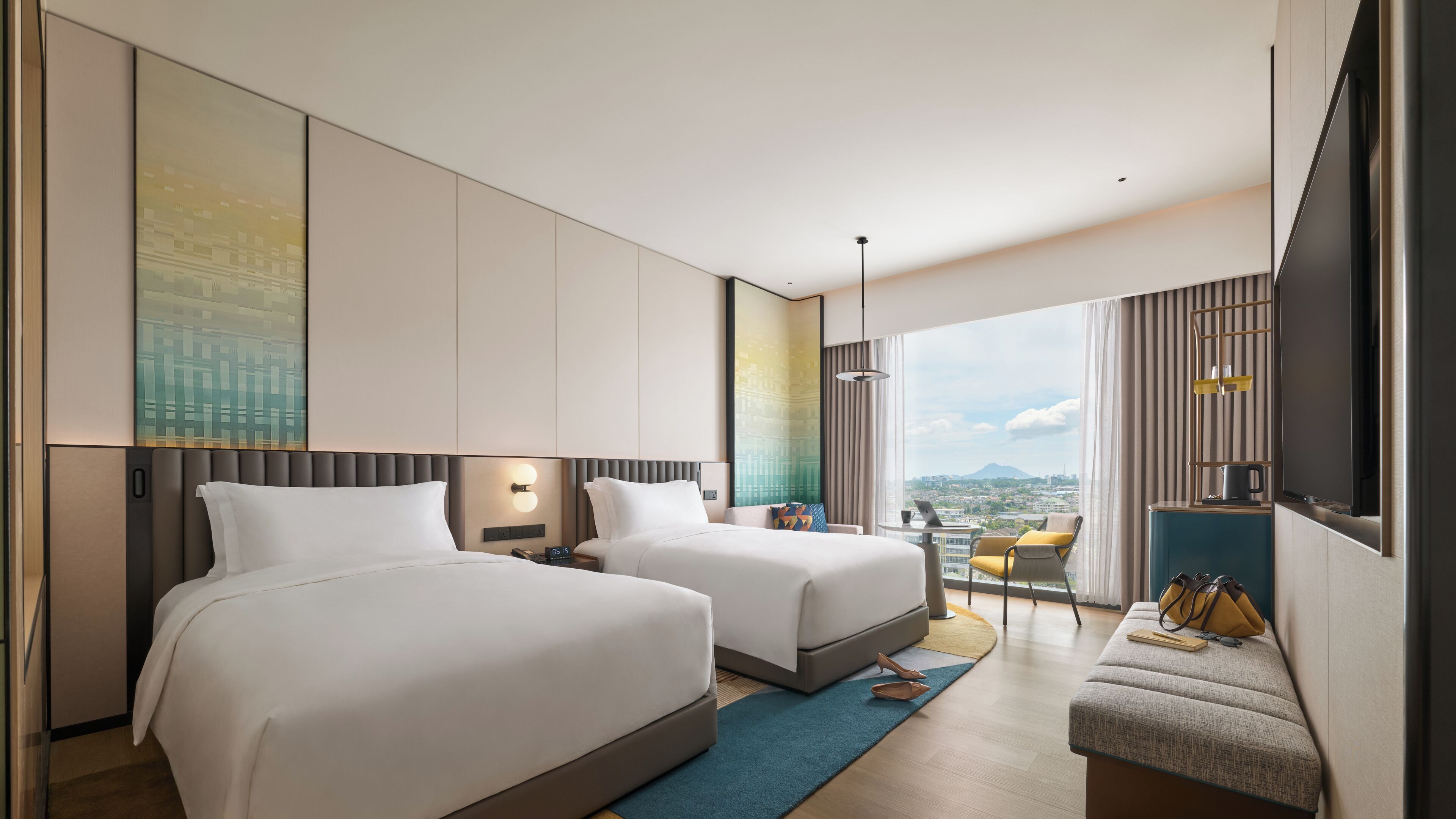 Quarto de hotel moderno com duas camas, área de estar e vista para a cidade.