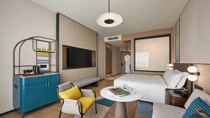 A modern hotel room with a bed, a seating area with a sofa and armchair, a small round table, a TV mounted on the wall, and a wardrobe. - Voco Kuching by IHG (Kuching)