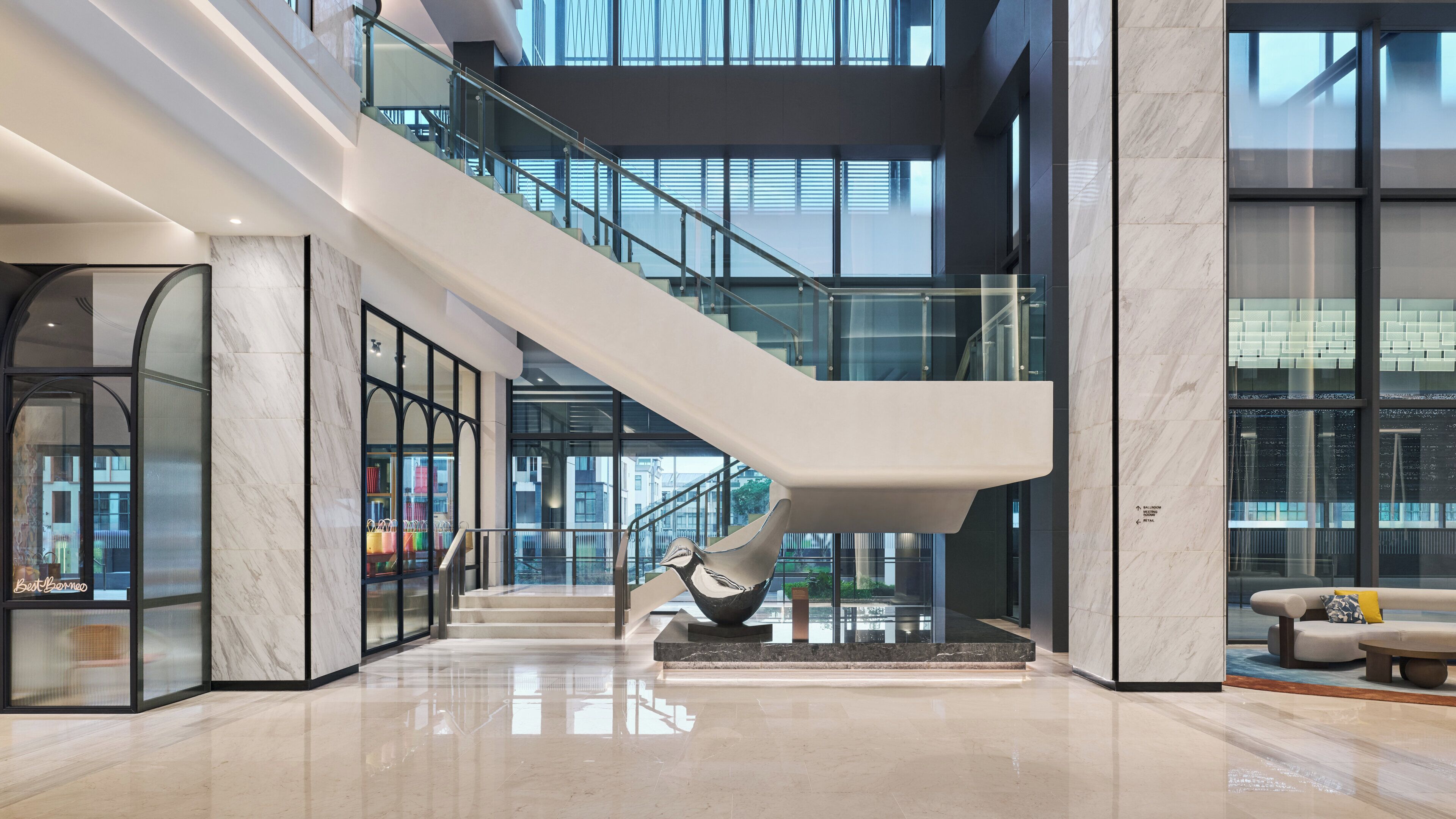 Un interior moderno con una escalera de cristal, suelo de mármol y vistas al exterior.