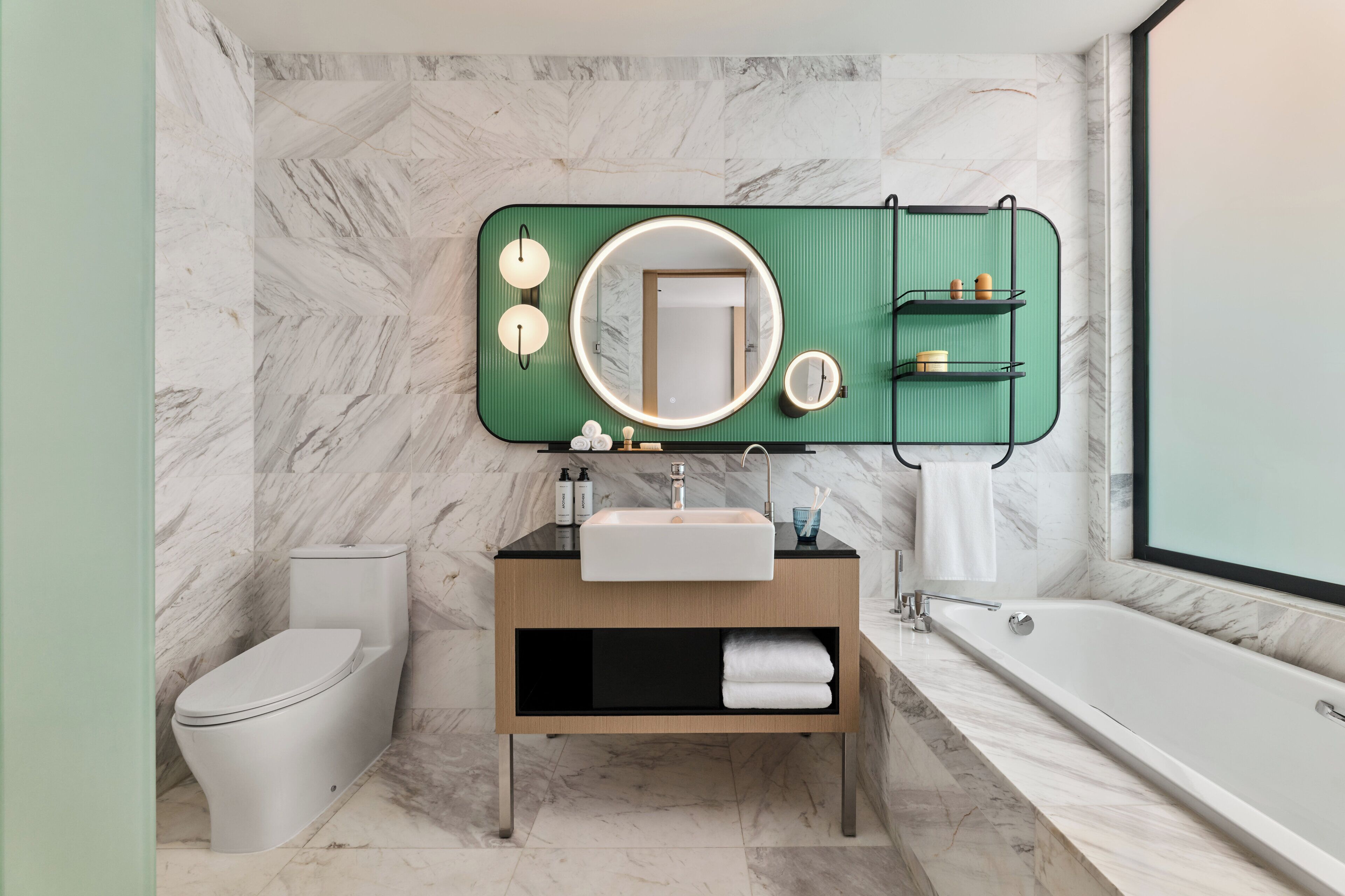 A modern bathroom with a marble wall, a green vanity with a sink, a toilet, and a bathtub.
