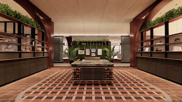 A hotel lobby with a central reception desk, green plants on shelves, framed pictures on the wall, and patterned flooring.