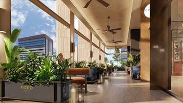 Un moderno hall de hotel con una zona de estar central, plantas en macetas y un bar a la derecha.