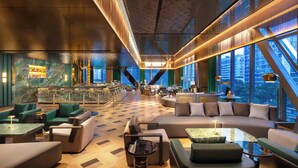 Un área de estar moderna con asientos, un bar y grandes ventanales con vistas a la ciudad.