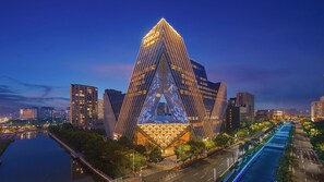 A modern hotel with a distinctive triangular facade, surrounded by a water body and urban skyline. - Hotel Indigo Ningbo By Ihg (Ningbo)