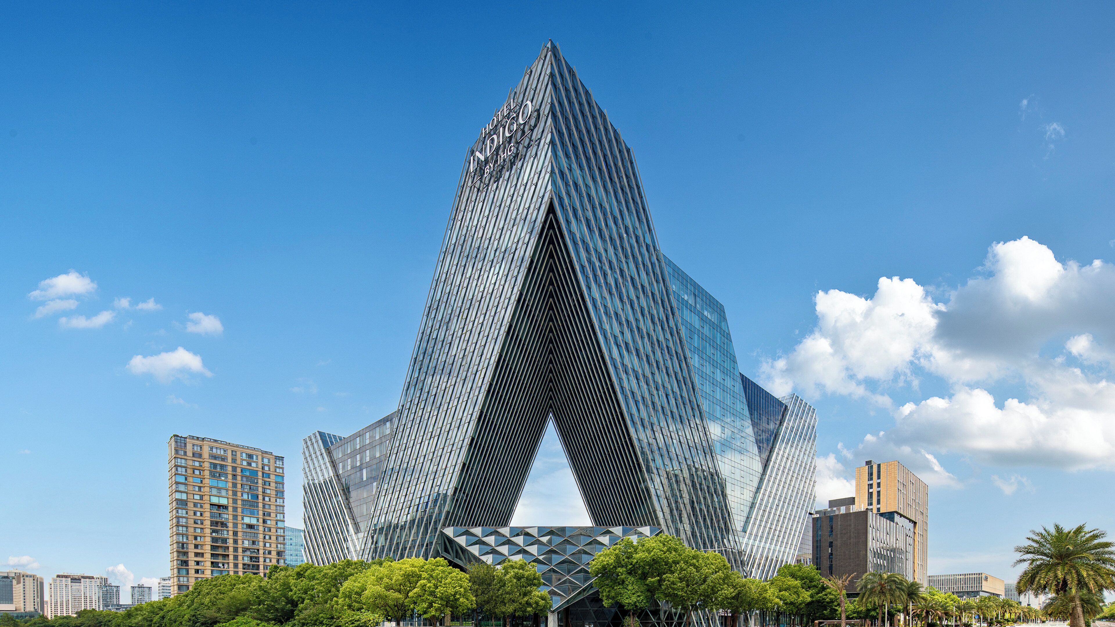 A modern hotel with a distinctive angular design, surrounded by other buildings and trees.