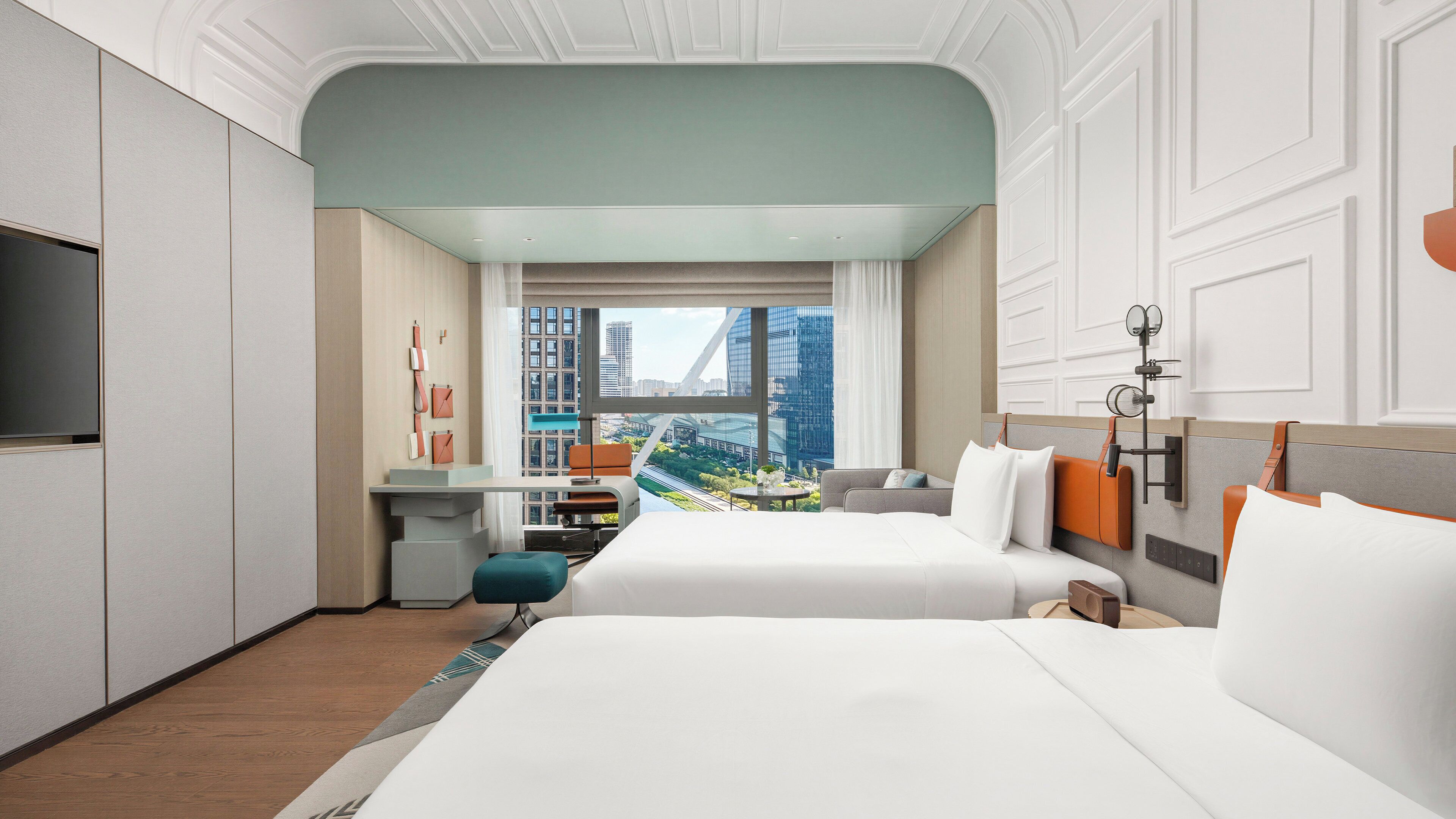 A hotel room with a large bed, a desk, a chair, and a view of a cityscape.