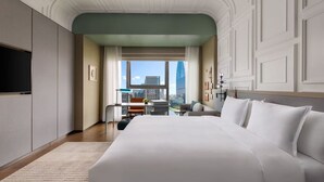 Habitación de hotel con una cama grande, un escritorio con silla, vista a la ciudad y un televisor en la pared.