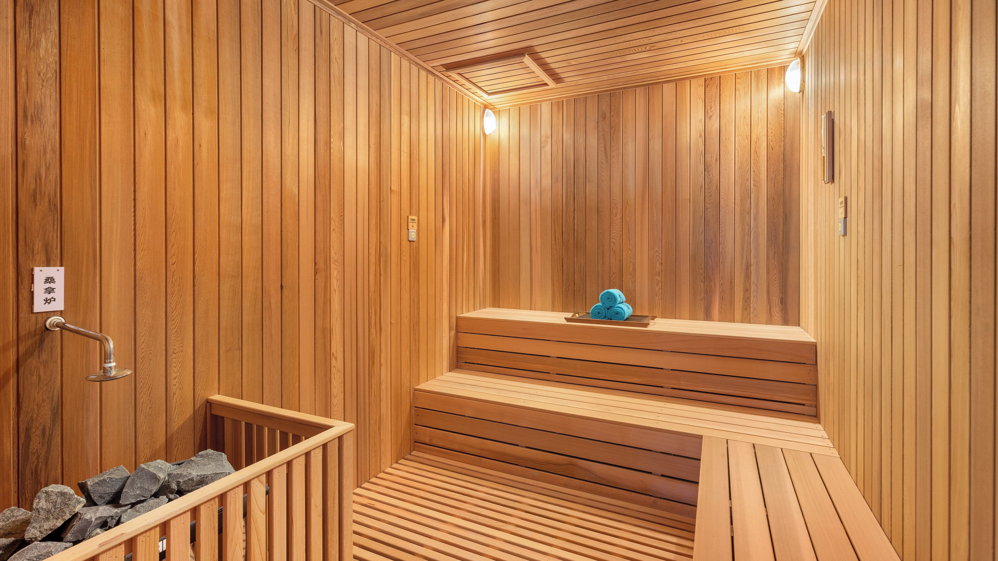 Un sauna en bois avec un banc, une petite table avec des serviettes et un récipient rempli de pierres.