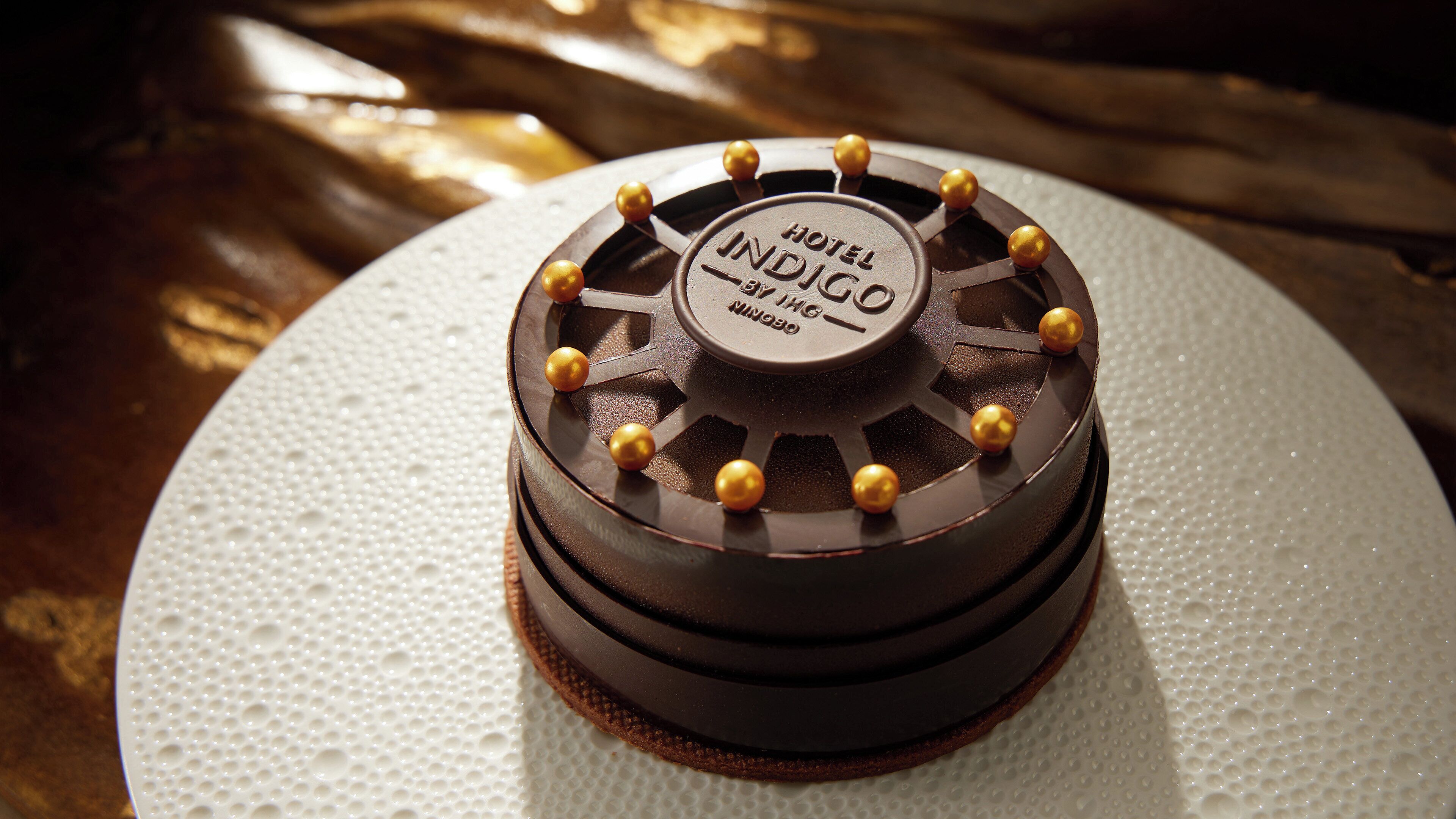 Un gâteau au chocolat, sur lequel est posée une étiquette, est présenté sur une assiette blanche.