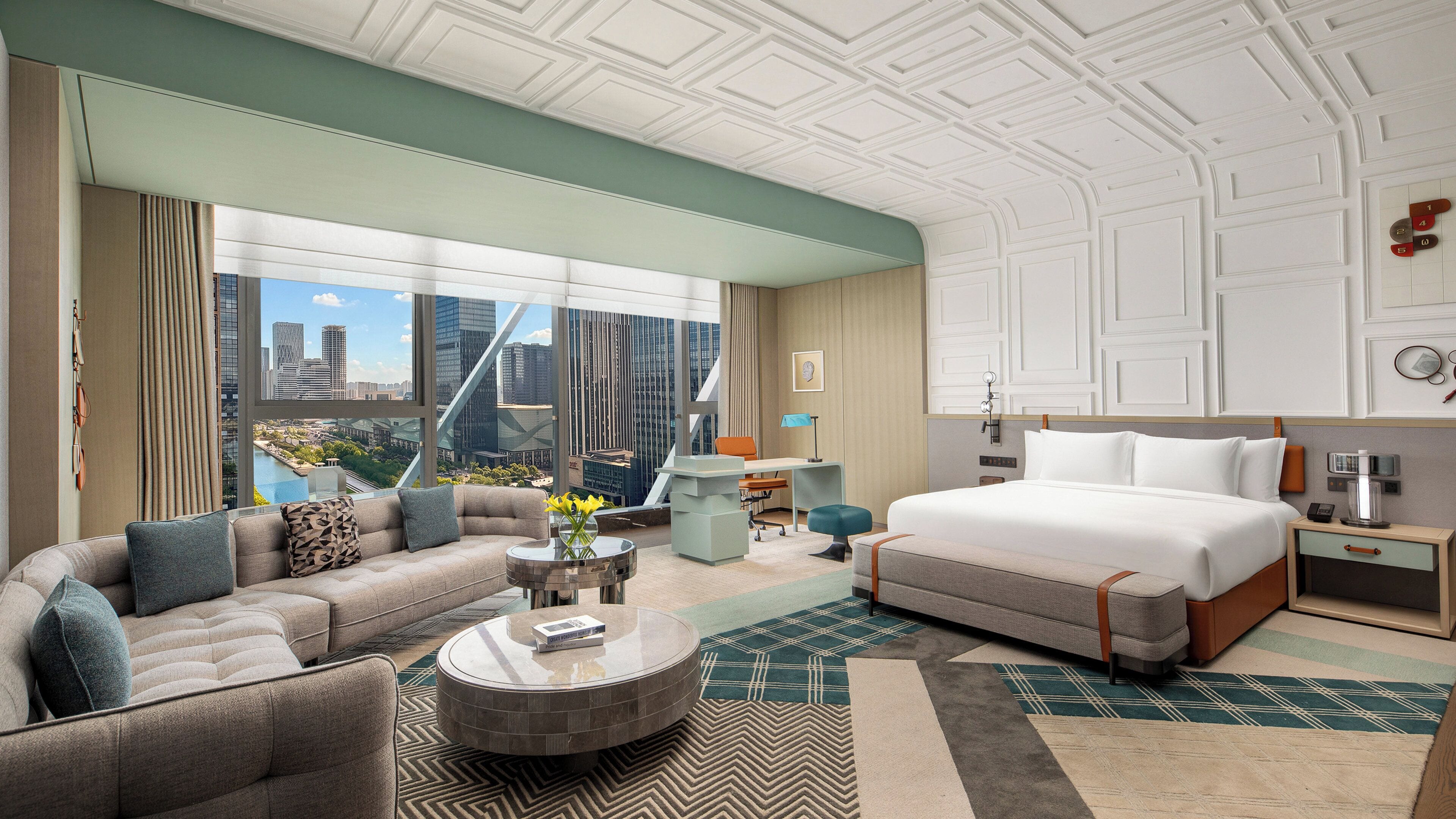 A modern hotel room with a large bed, a sofa, a desk, and a view of the cityscape.