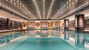 Una amplia piscina interior de diseño moderno, rodeada de zonas de estar y un muro de piedra.