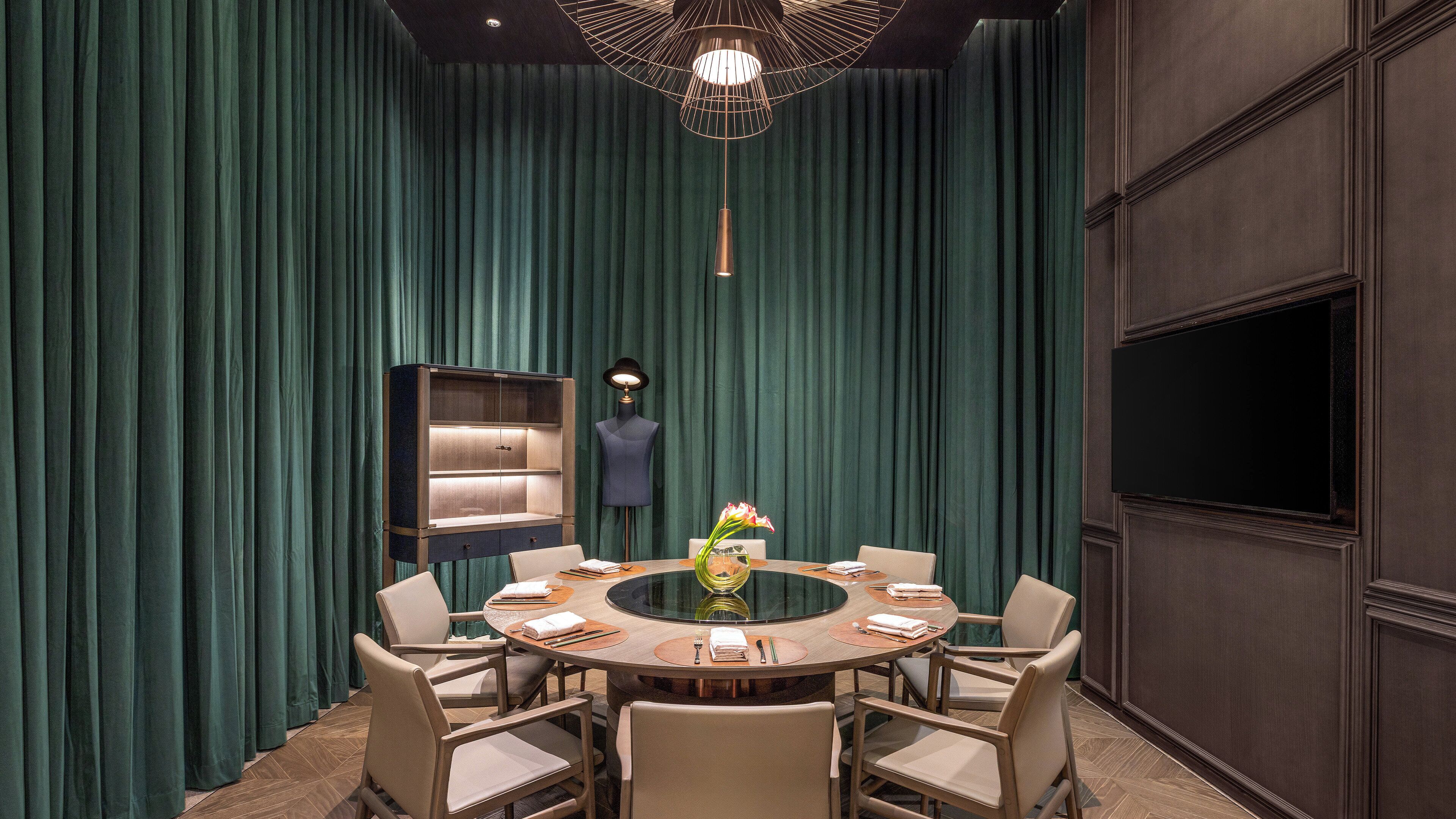 A conference room with a round table, chairs, a mannequin, and a TV on the wall.