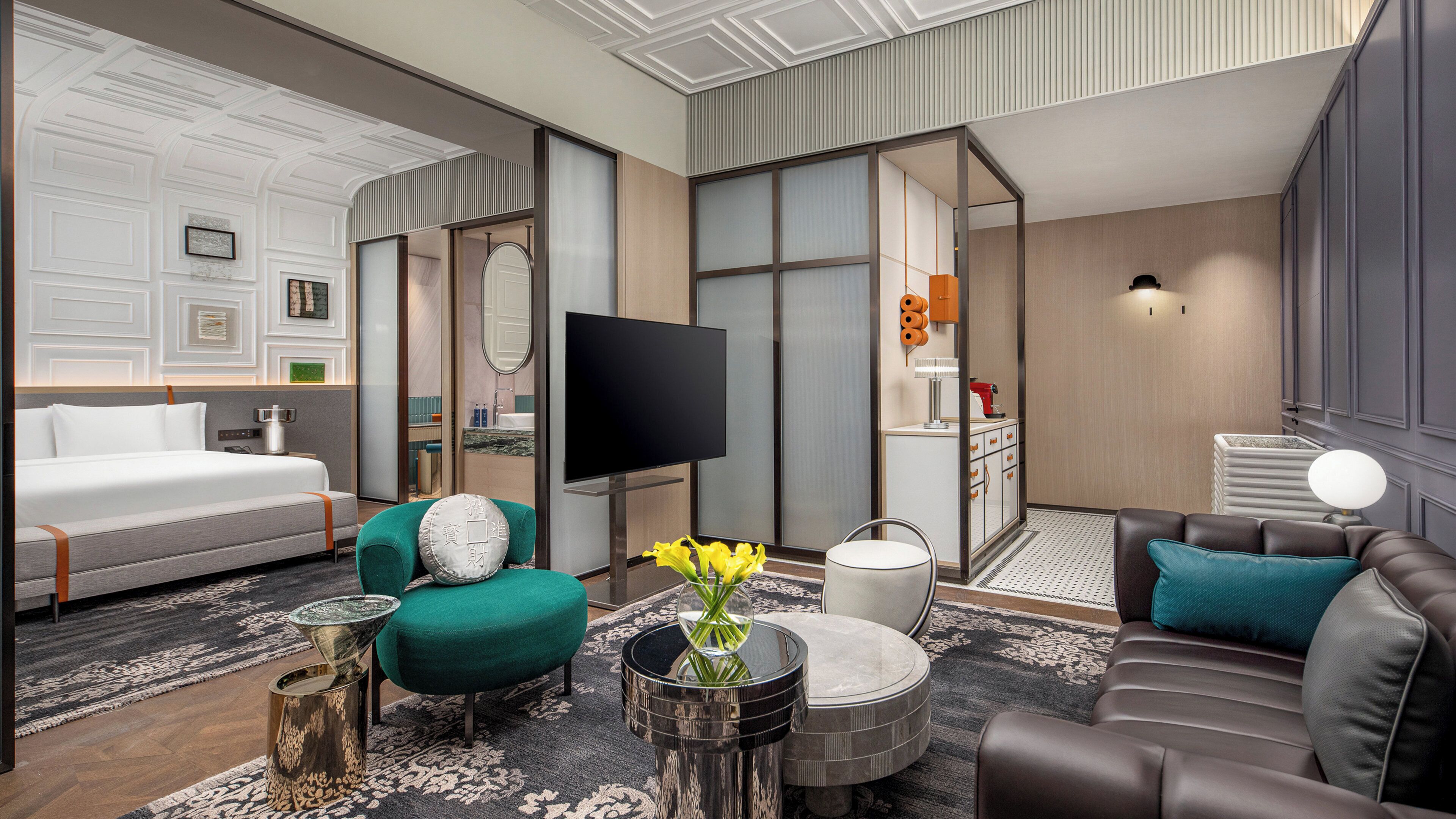 A modern hotel room with a bed, seating area, TV, and a bathroom visible through a glass partition.