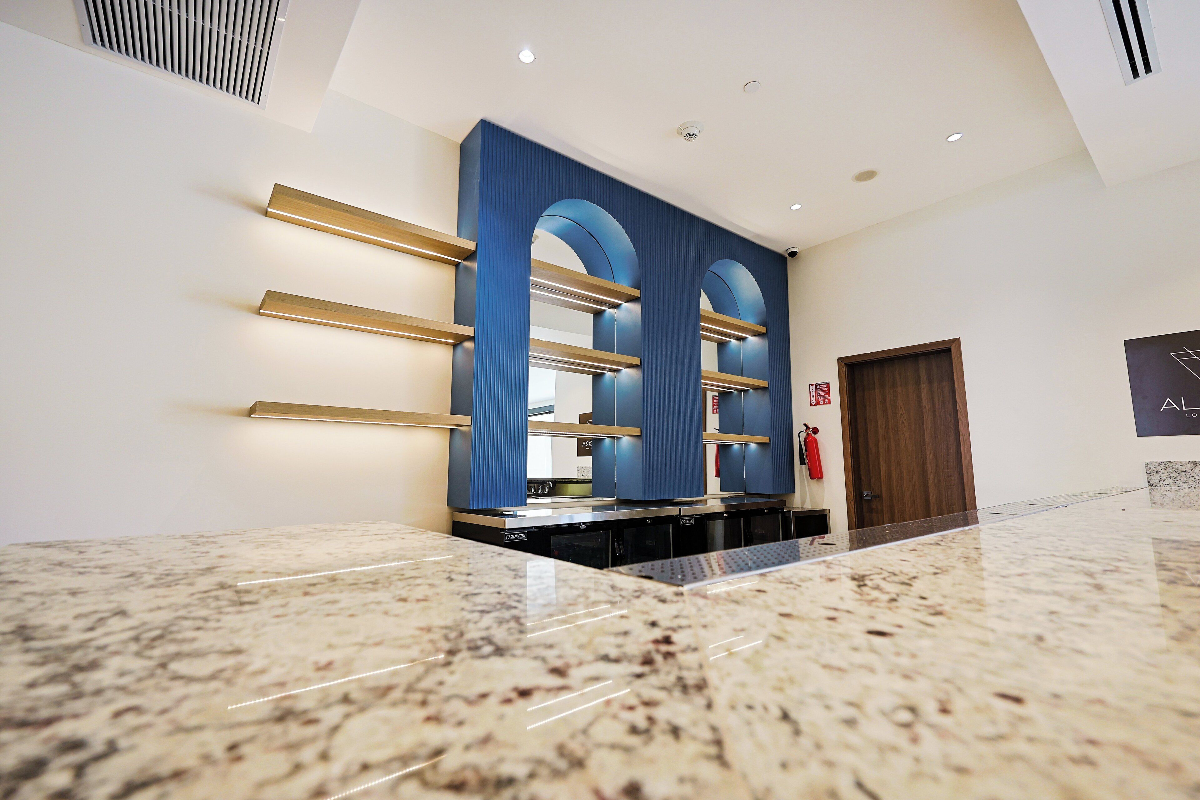 A modern lobby with a marble floor, blue and gold decor, and a fire extinguisher on the wall.