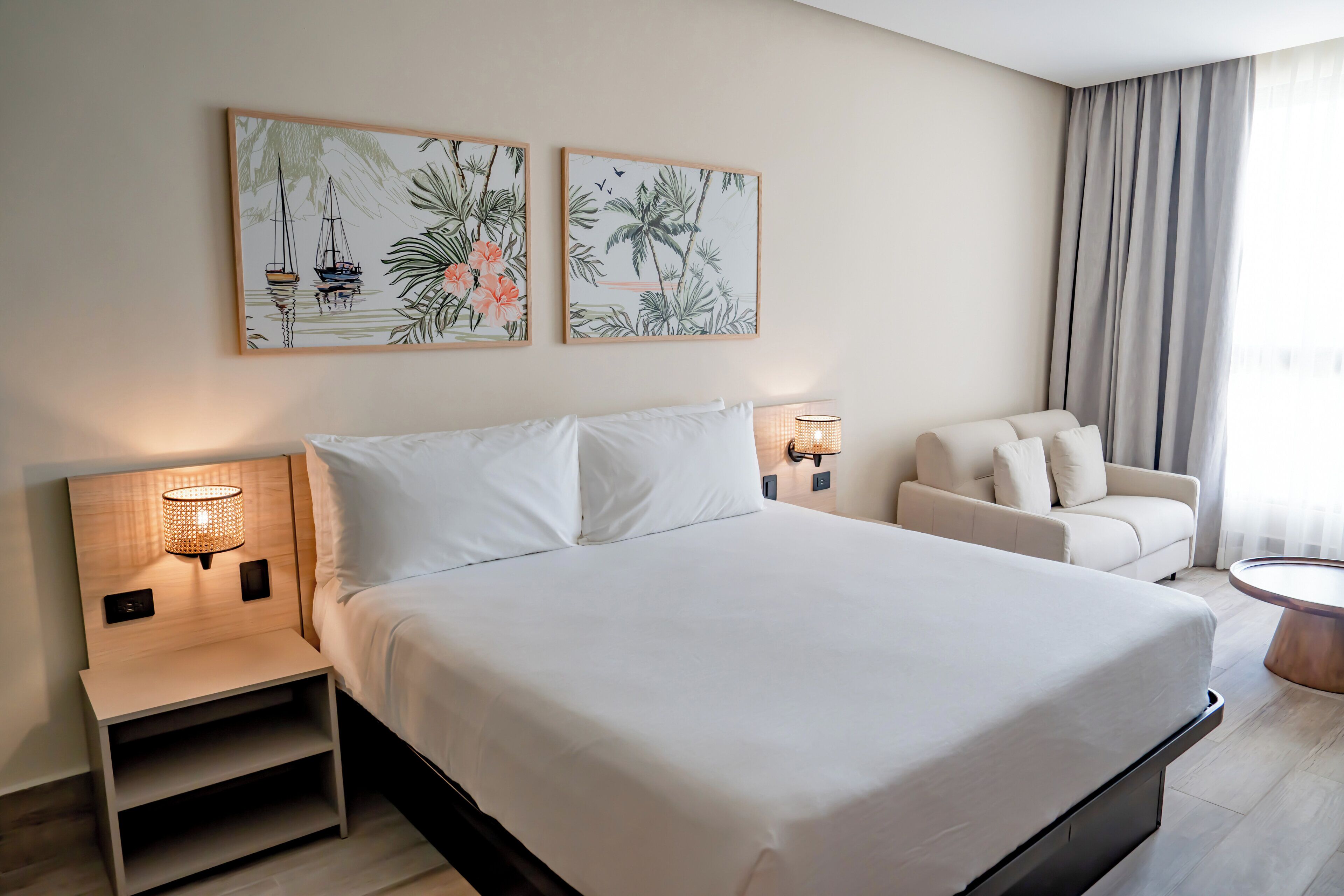 A hotel room with a large bed, a nightstand with a lamp, a sofa, and two wall-mounted lamps.