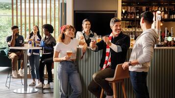 A group of people toasting at a bar with a modern interior, including a bar counter and seating area.