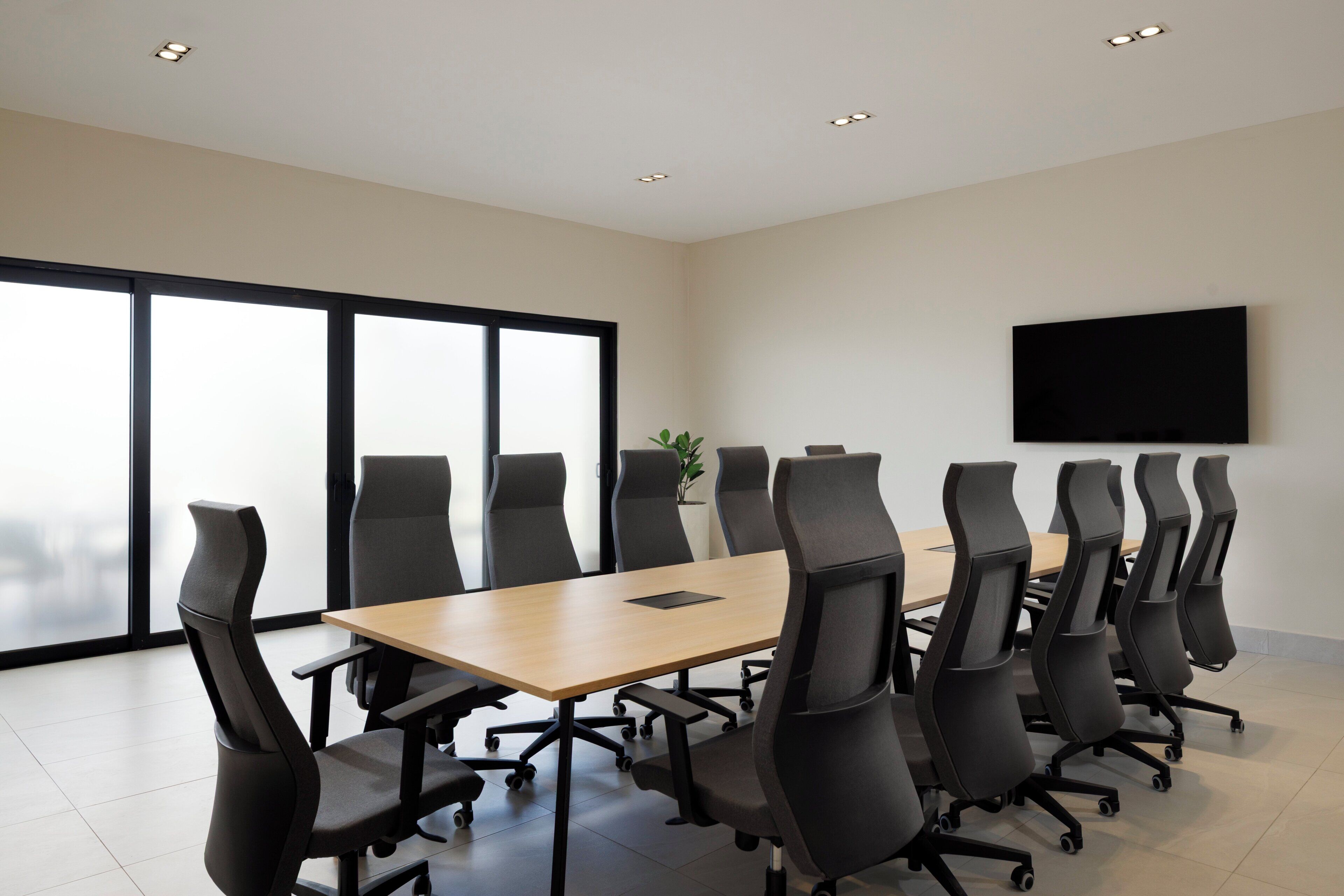 Une salle de conférence avec une longue table et de nombreuses chaises, une grande fenêtre et un téléviseur à écran plat fixé au mur.