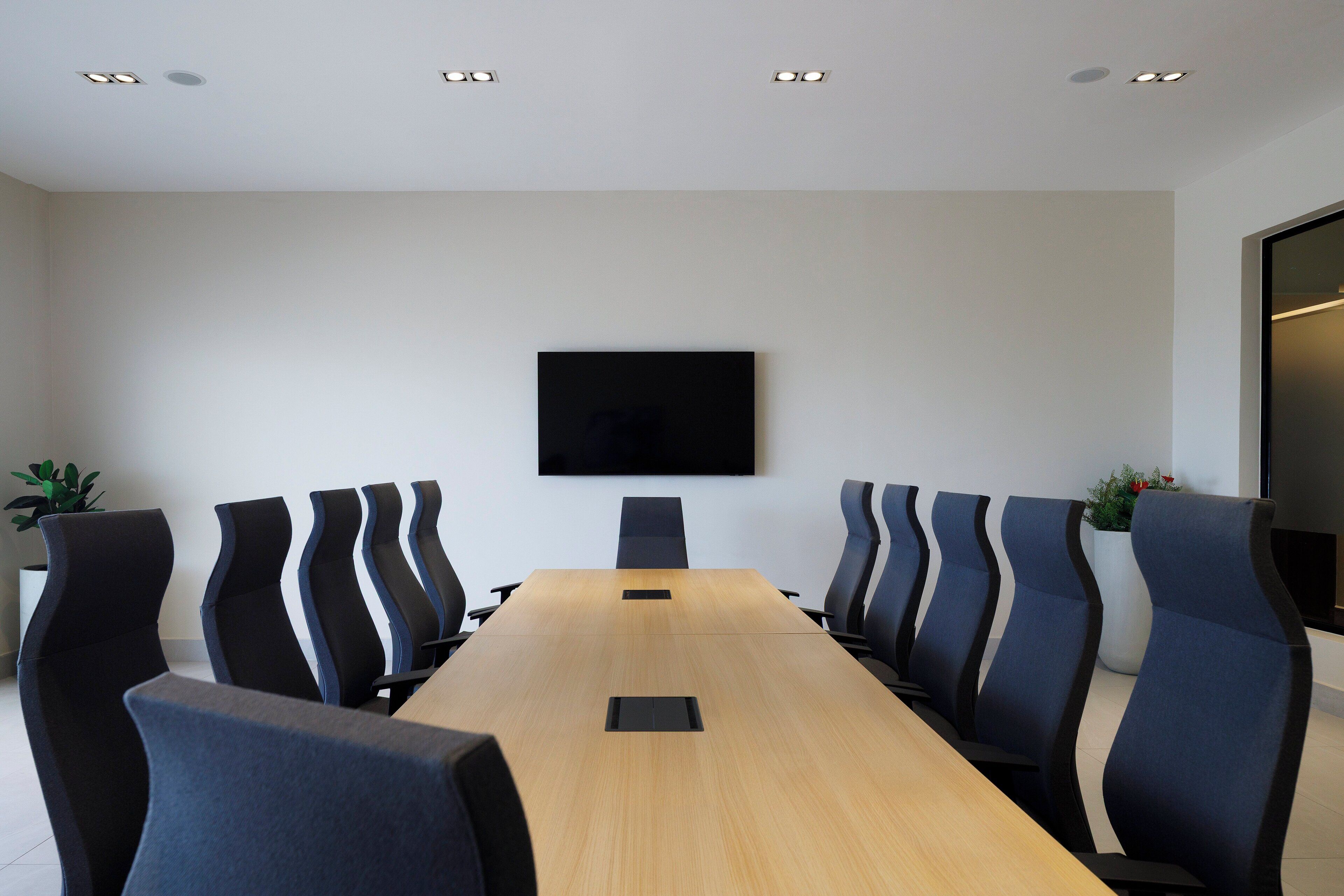 Une salle de conférence avec une longue table et des chaises, un téléviseur à écran plat fixé au mur et des luminaires au plafond.
