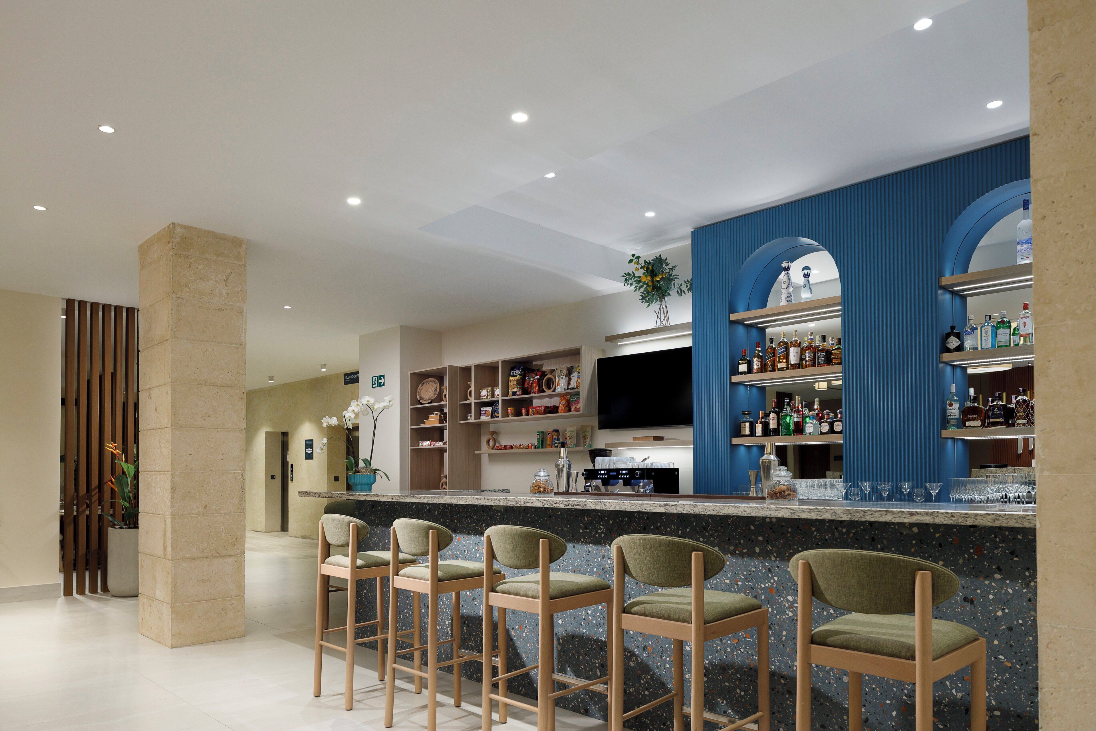 A modern bar area with a granite countertop, bar stools, and a variety of liquor bottles.