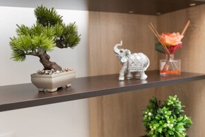 Ein Regal mit einem Bonsai-Baum, einer Elefantenfigur und einer Blumenvase.