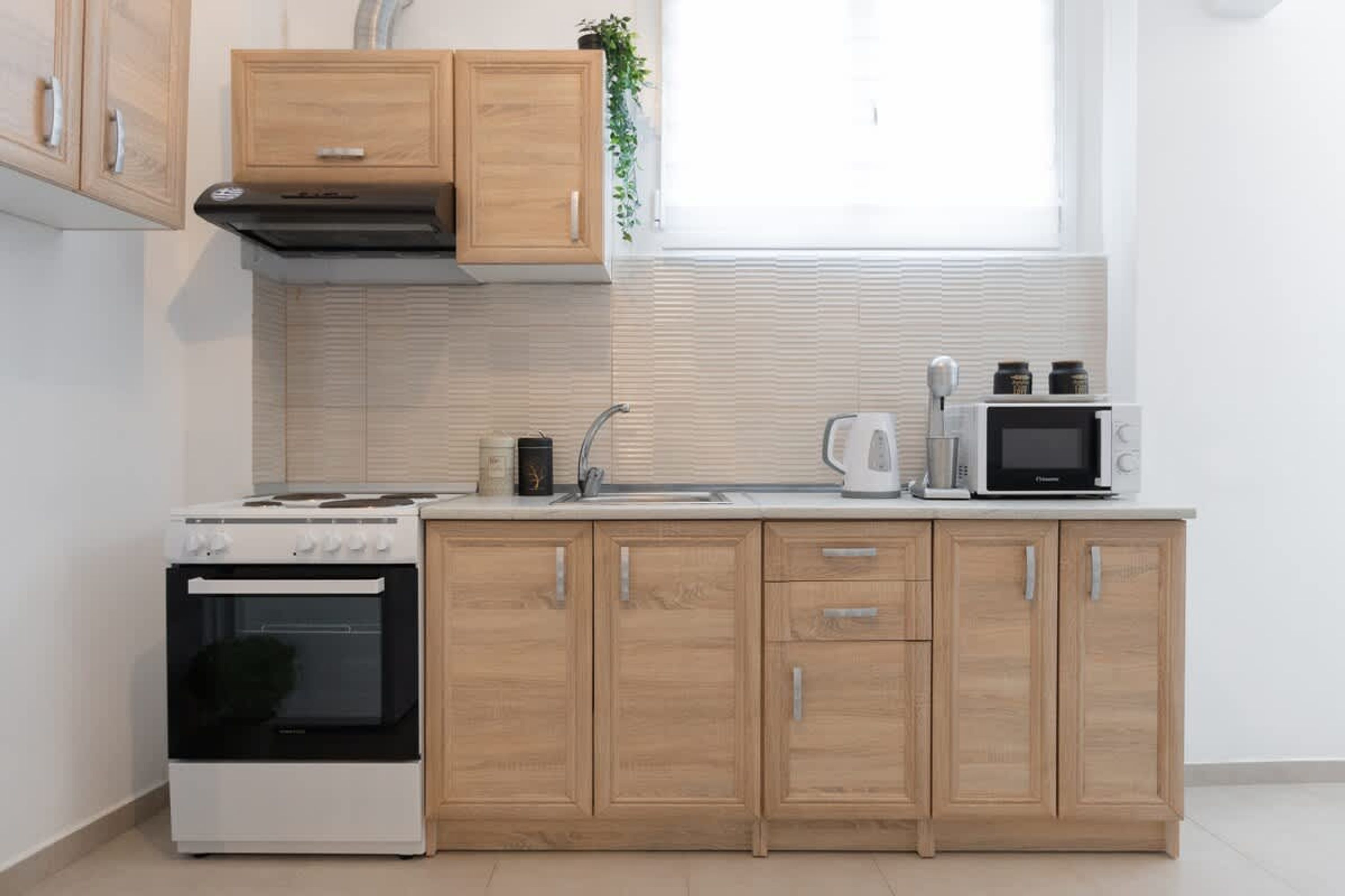 A modern kitchen with wooden cabinets, a stove, a microwave, and a kettle.