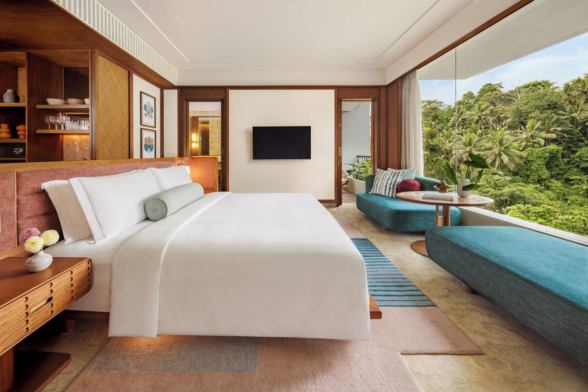 Ein modernes Hotelzimmer mit einem großen Bett, einer Sitzecke, einem Fernseher und Blick auf üppiges Grün.