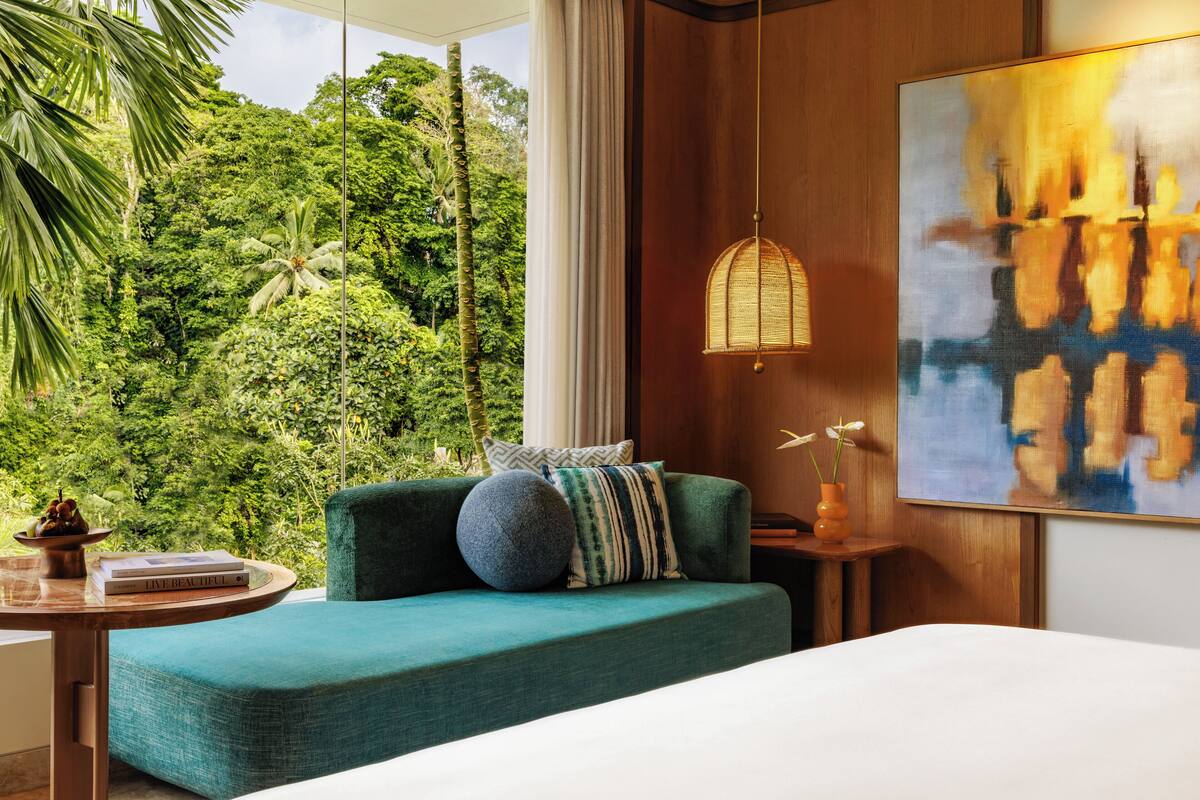 Une chambre moderne avec un grand lit, un canapé de couleur turquoise et une vue sur une végétation luxuriante.