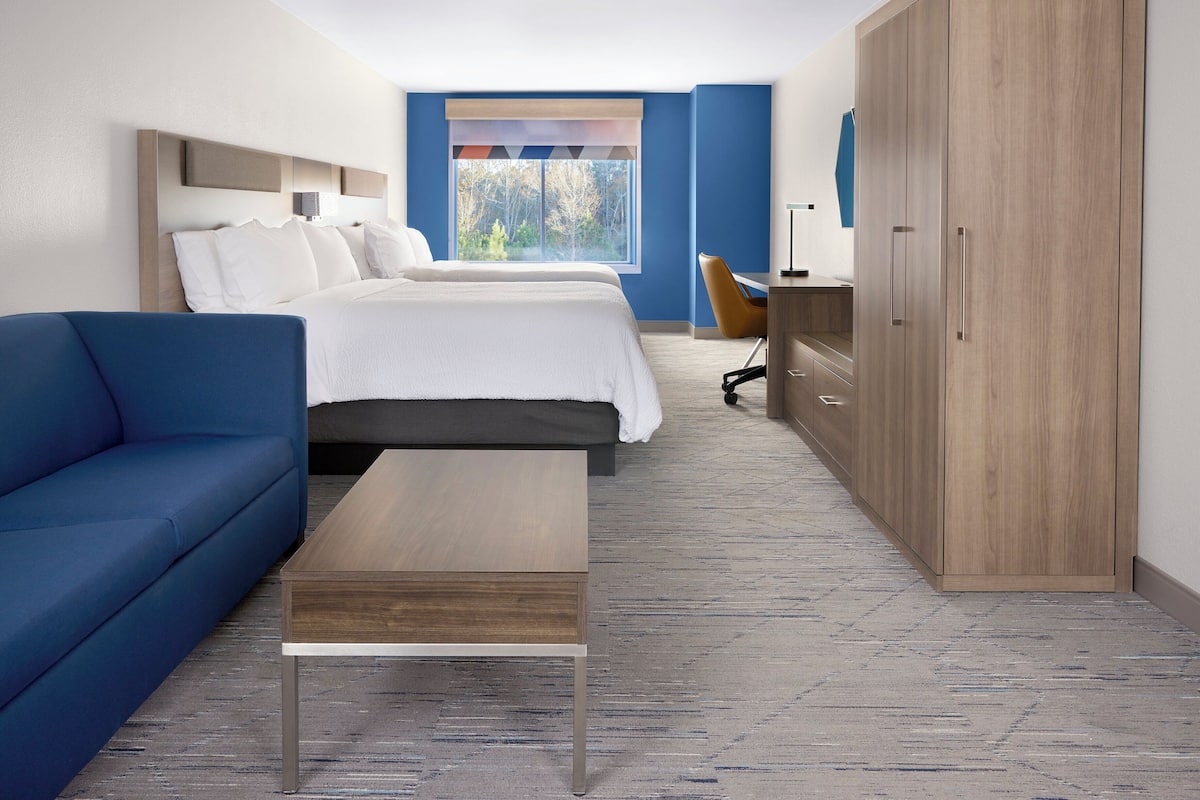A hotel room with a bed, a blue sofa, a wooden desk, and a wardrobe.