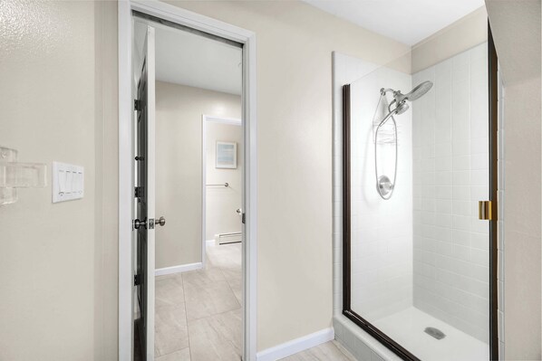 A modern bathroom with a glass-enclosed shower, a white tiled wall, and a door leading to another room.