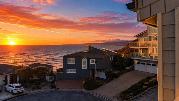 Un quartier résidentiel situé sur la côte, avec une maison dotée d’un garage, d’une allée et offrant une vue sur l’océan au coucher du soleil.
