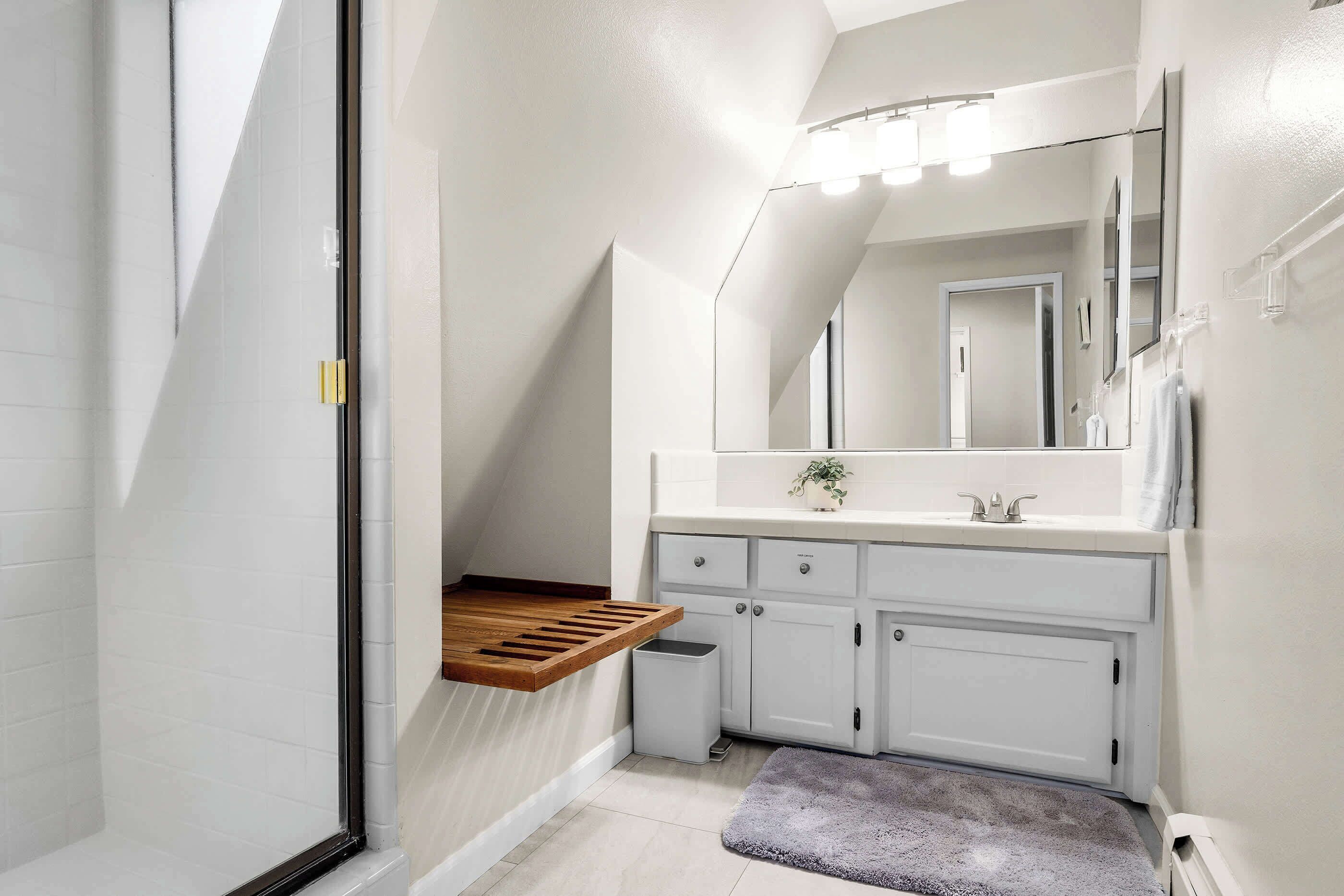 A modern bathroom with a shower, a wooden shelf, a sink, and a large mirror.